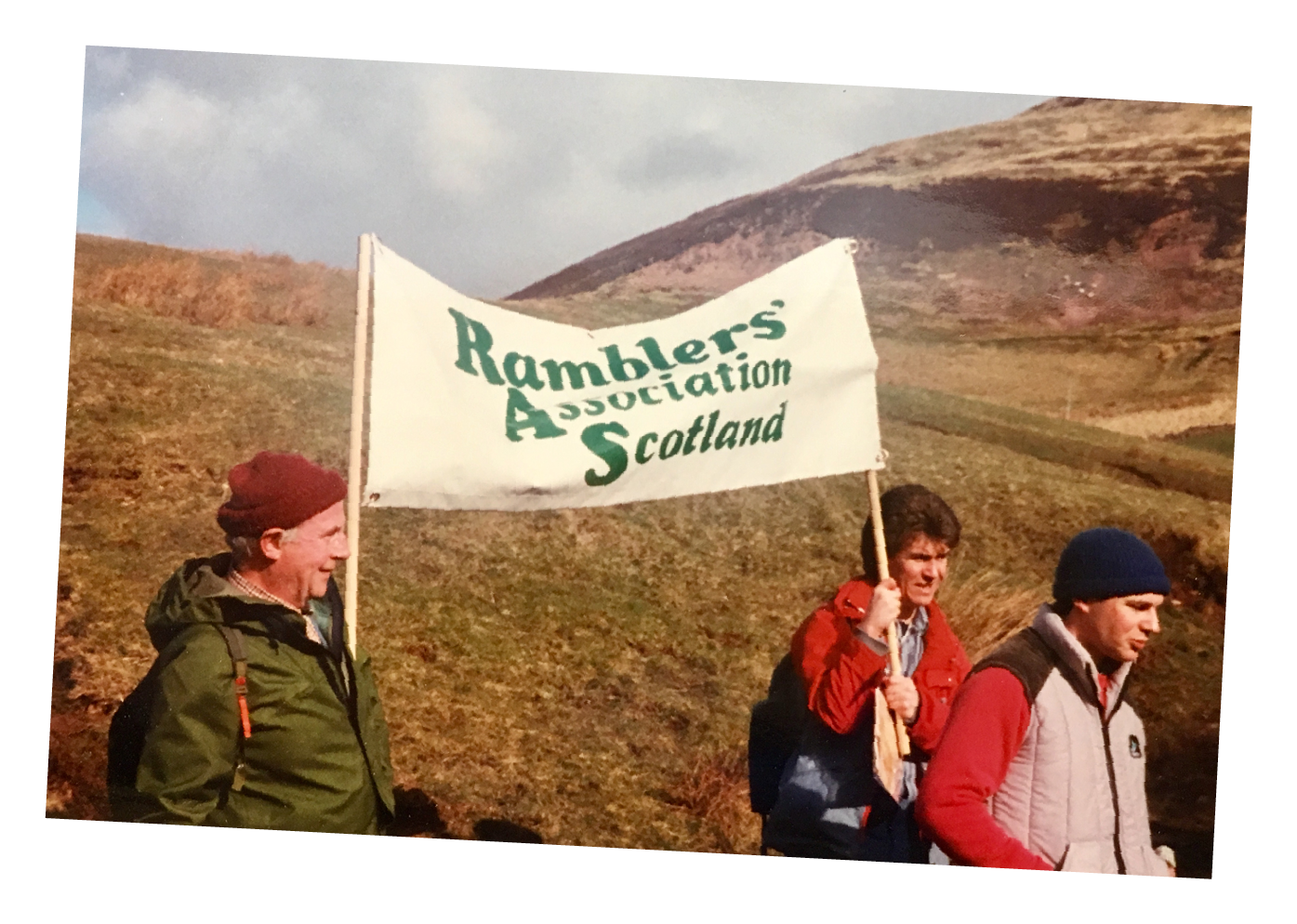 Three ramblers holding a sign saying: Ramblers' Association Scotland