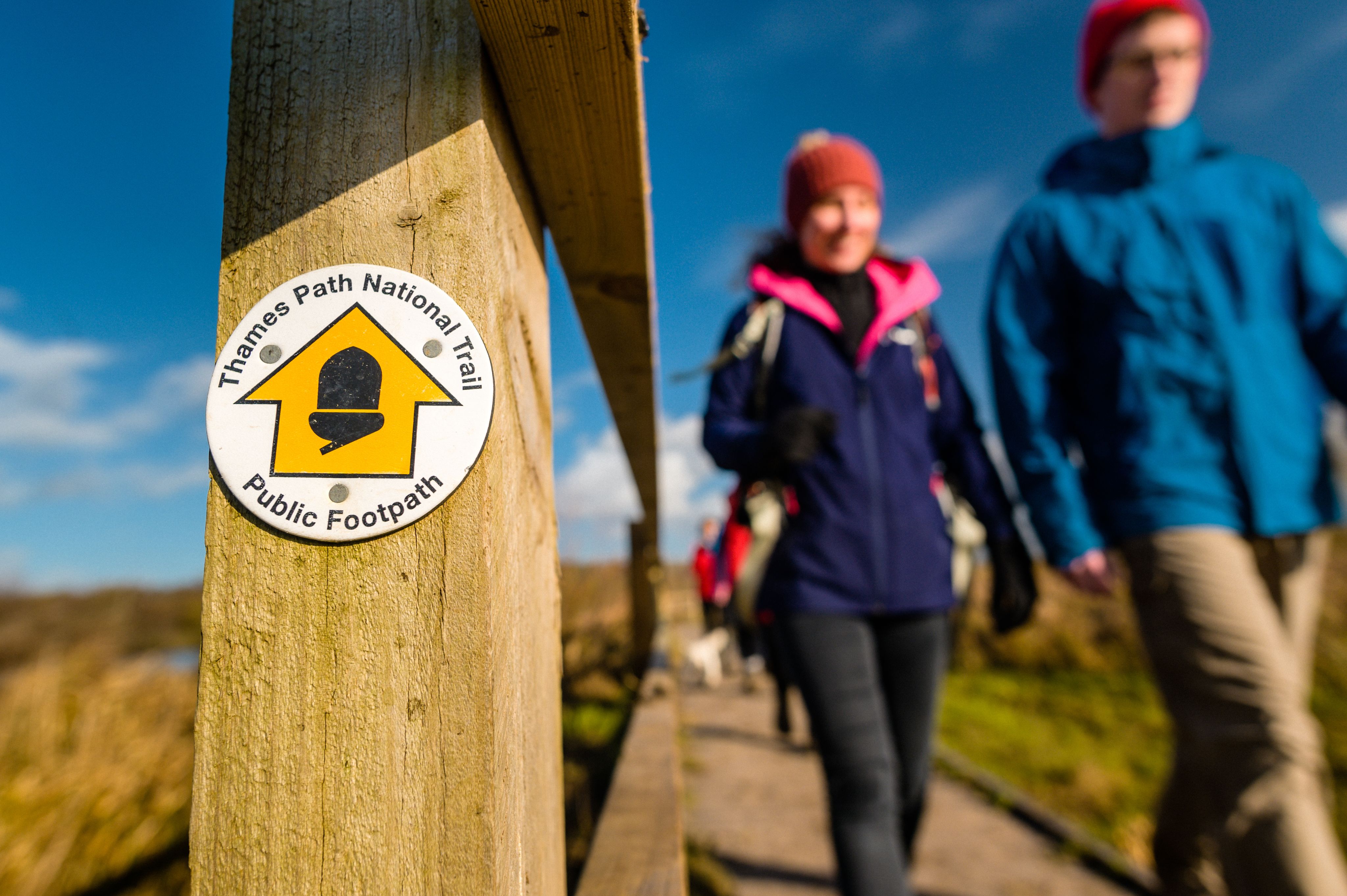 Thames Path National Trail waymarker with ramblers walking past in background