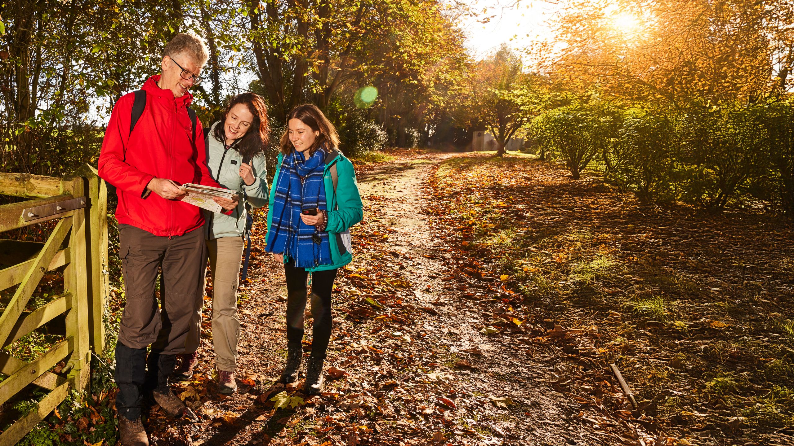 Three ramblers smiling and looking at a map in a wooded area