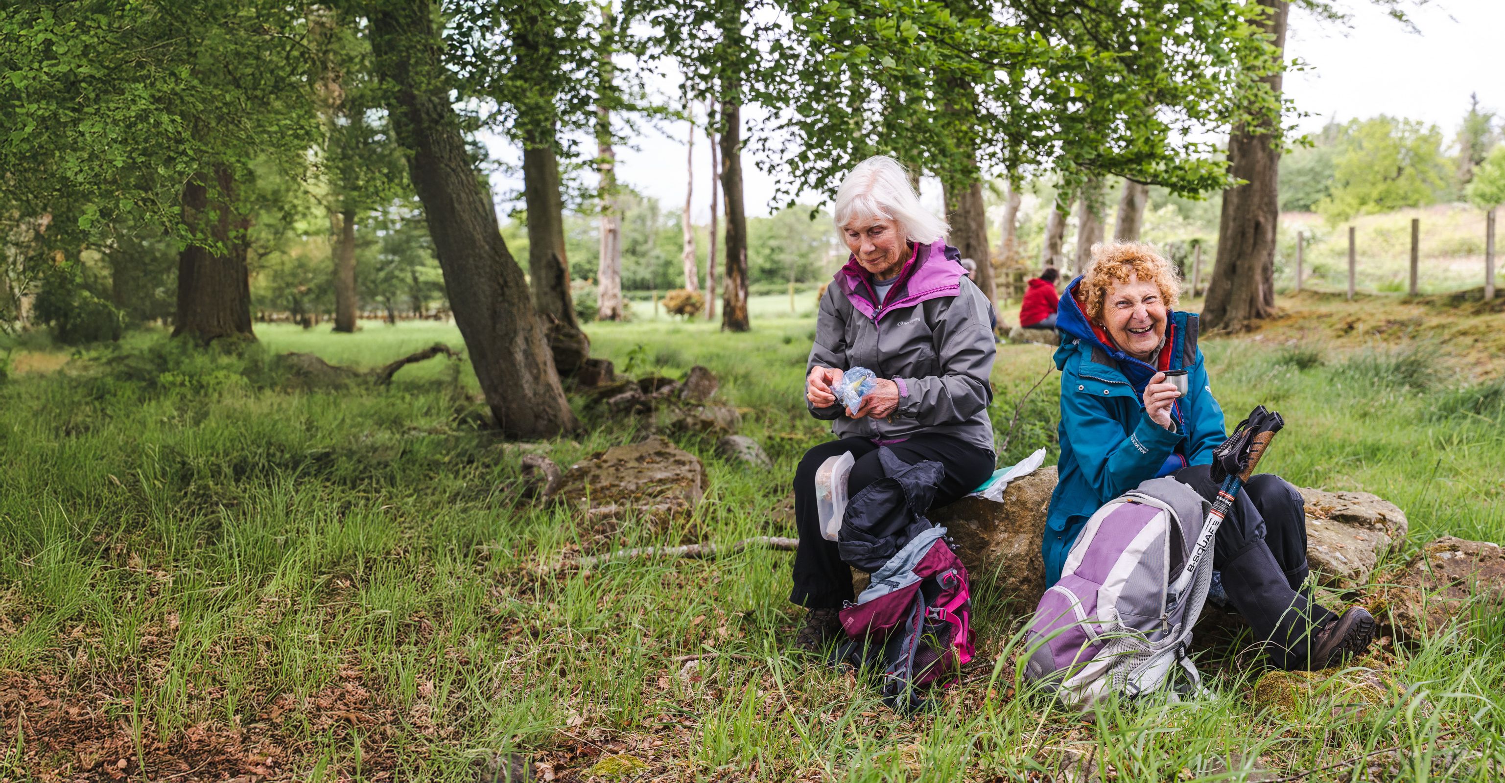 Two older women ramblers stopping for a snack and smiling