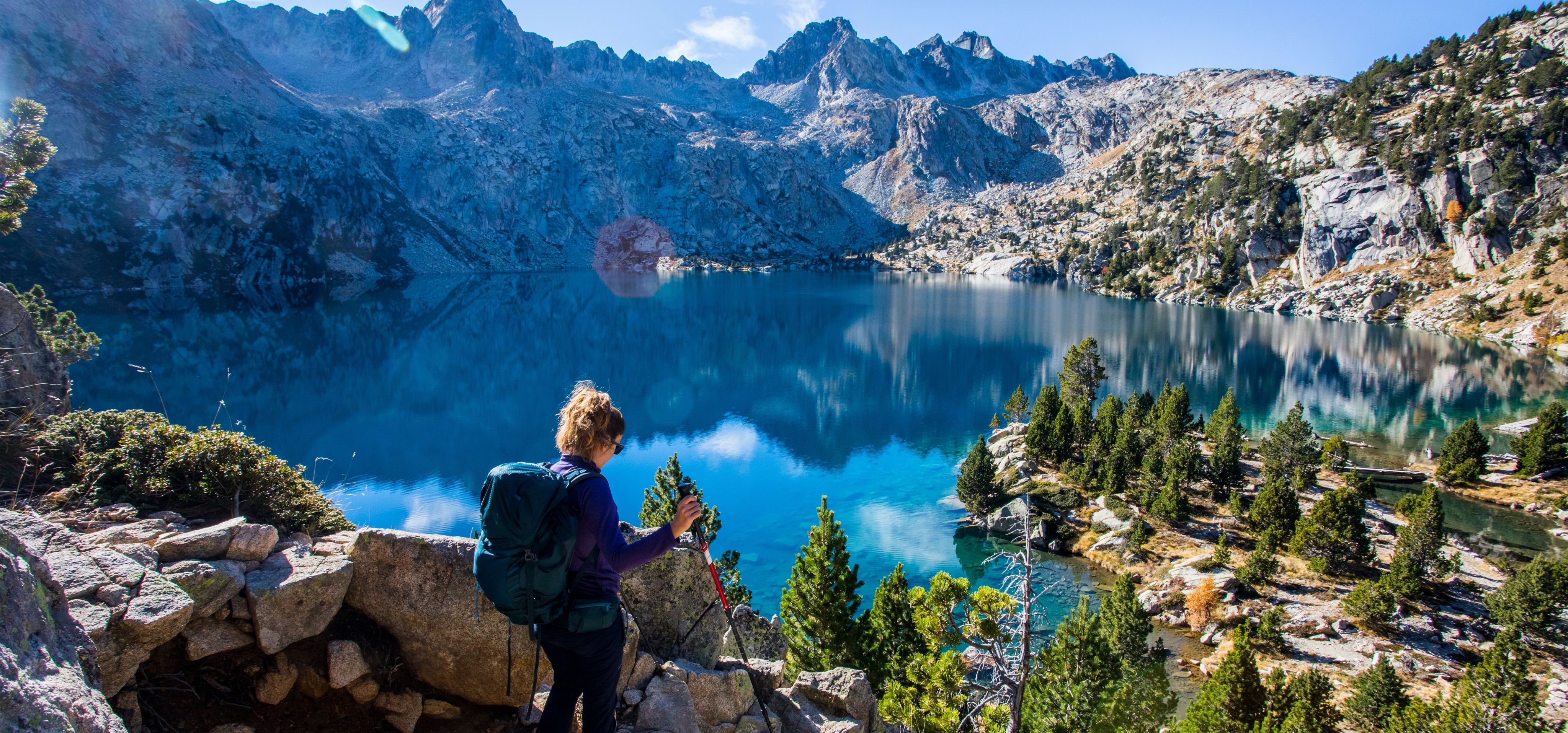 Woman with poles and rucksack standing in woods with her eyes closed and smiling