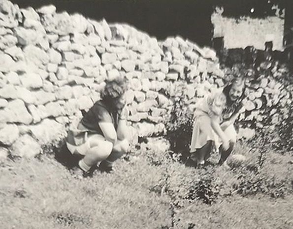 Two women crouching behind a wall in 1940s Malham Dale, North Yorkshire
